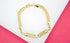 A gold curb chain bracelet featuring an ID plate centered with a sparkling diamond lies against a white and pink background.