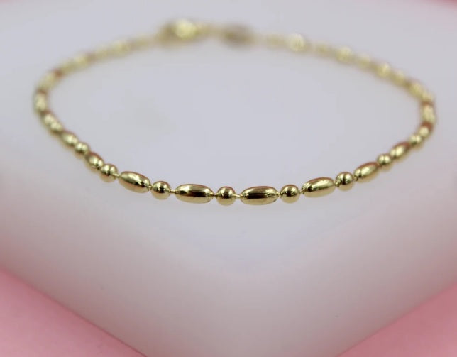 A delicate gold beaded bracelet rests on a smooth white display surface.