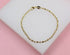 A delicate gold beaded bracelet rests on a white display surface against a pink background.