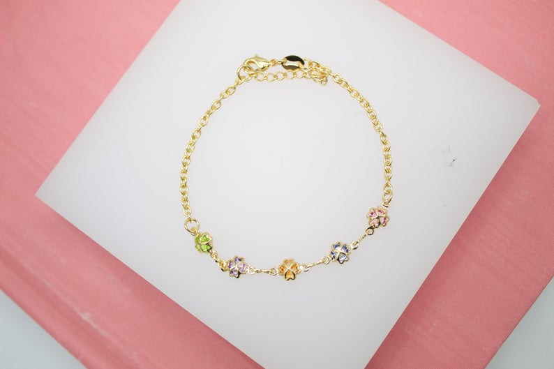 A delicate gold chain bracelet features colorful, crystal-embellished four-leaf clover charms displayed on a white surface.