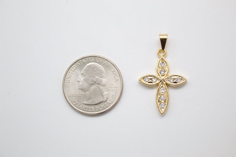 A gold cross pendant encrusted with small cubic zirconia stones rests next to a US quarter coin to show its scale.