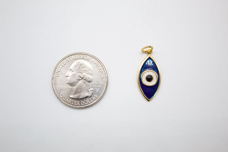 A gold evil eye charm rests next to a US quarter coin for size comparison on a white background.
