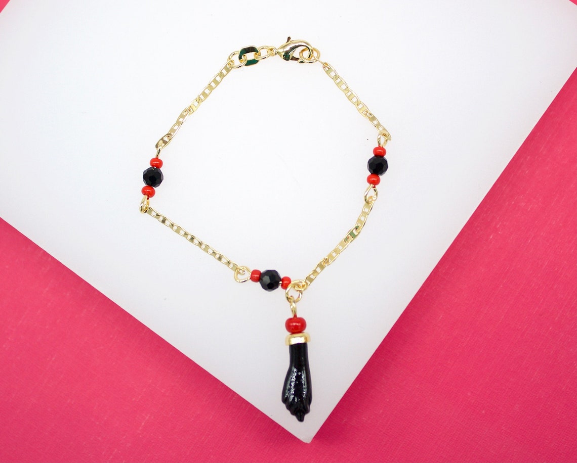 A delicate gold chain bracelet features black and red beads, accented with a figa charm pendant.
