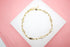 A delicate gold chain bracelet features alternating tiny elephant charms and small beads, resting on a white display against a pink background.