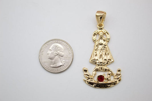 A gold religious pendant featuring the Virgin Mary and child stands next to a US quarter coin for scale on a light background.