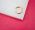 A polished gold clicker ring rests on a white display against a vibrant pink background.