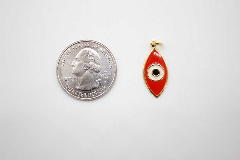 A red enamel evil eye charm rests beside a US quarter coin to show its size.