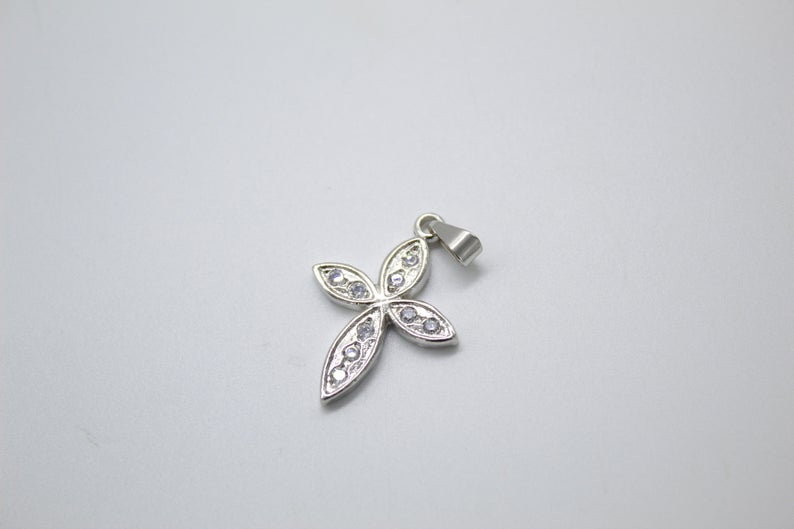 A delicate silver cross pendant embellished with sparkling cubic zirconia stones lies on a plain white surface.