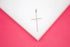 A silver cross pendant encrusted with sparkling rhinestones rests on a white display against a vibrant pink background.