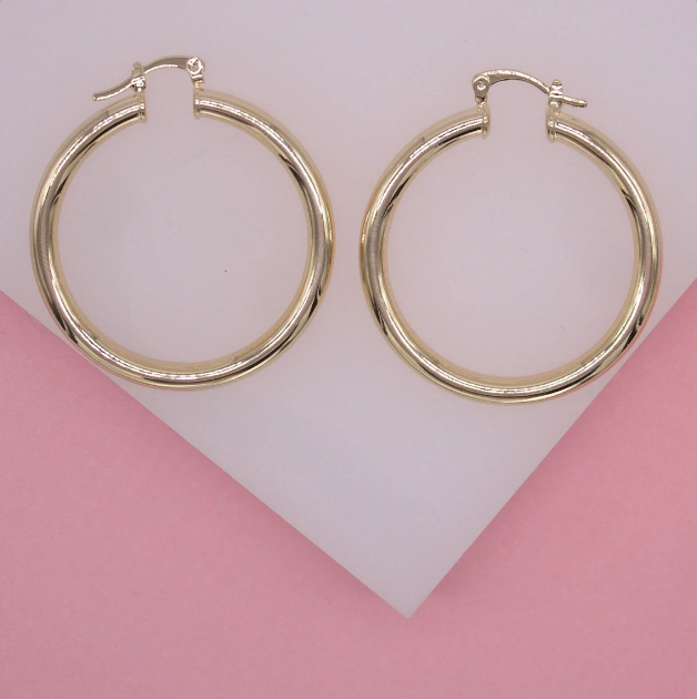 A pair of polished gold hoop earrings rests on a light pink and white display stand.