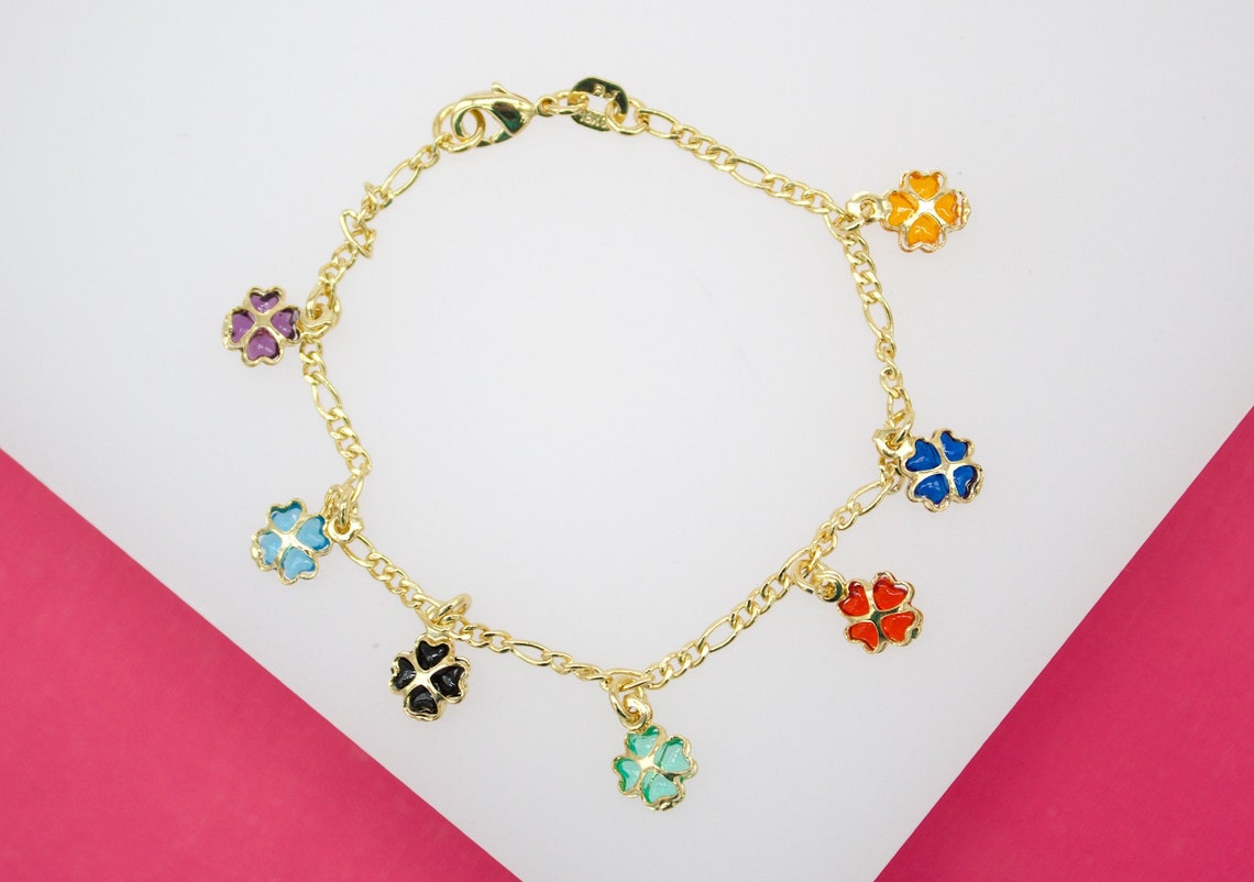 A gold chain bracelet features multiple colorful enamel four-leaf clover charms dangling against a white and pink background.