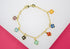 A gold chain bracelet features multiple colorful enamel four-leaf clover charms dangling against a white and pink background.