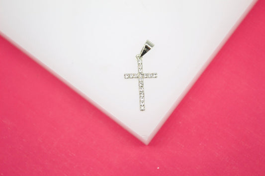 A sparkling rhinestone cross pendant rests neatly on a white display against a pink background.