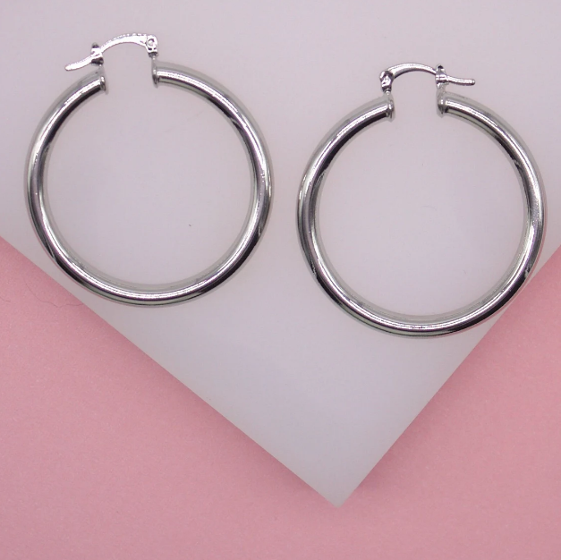 A pair of polished silver hoop earrings rests against a pink and white background.