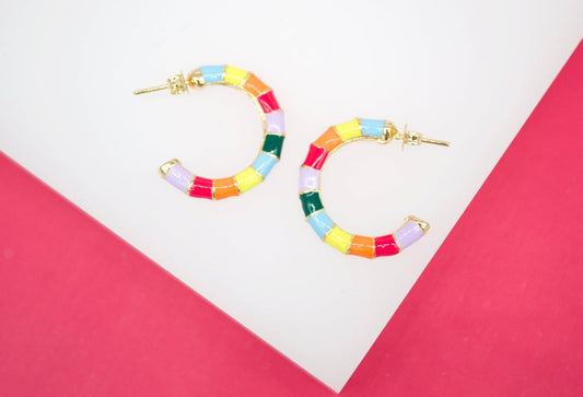 A pair of colorful, multi-striped enamel hoop earrings rests on a white and pink geometric display surface.