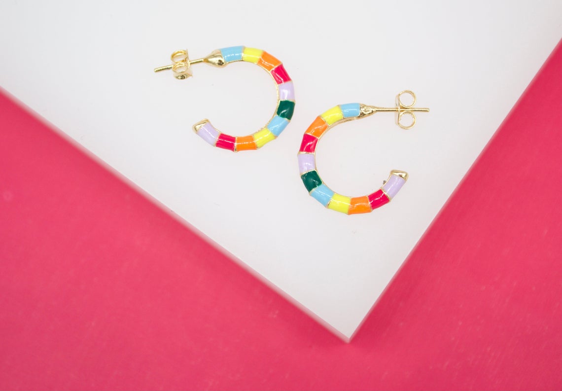 A pair of vibrant multicolored enamel hoop earrings rests on a white and pink display surface.