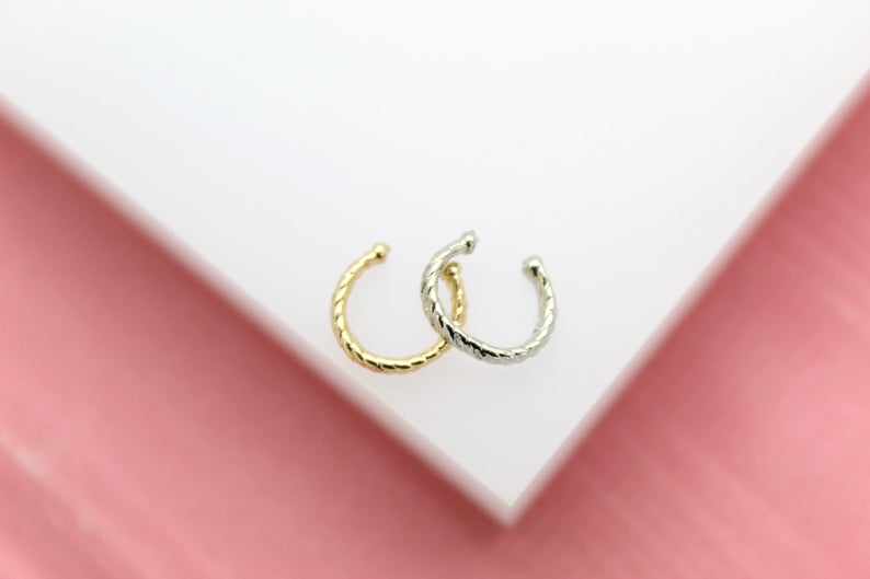 Two twisted metal ear cuffs in gold and silver rest on a white surface.