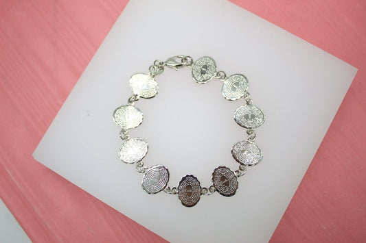A silver charm bracelet featuring multiple engraved oval medallions rests on a white display block.