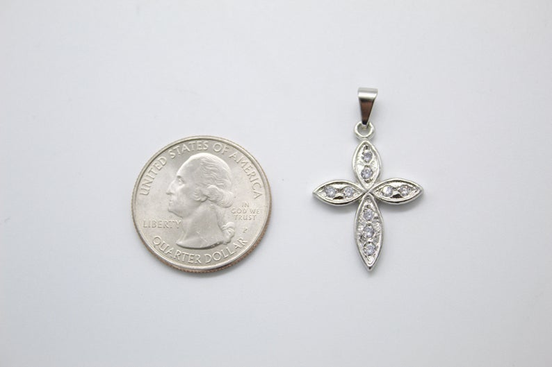 A sparkling diamond cross pendant sits next to a US quarter coin for size comparison on a light surface.