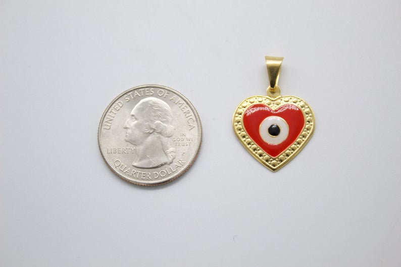 A gold heart pendant featuring a red and white evil eye design sits next to a US quarter for scale.