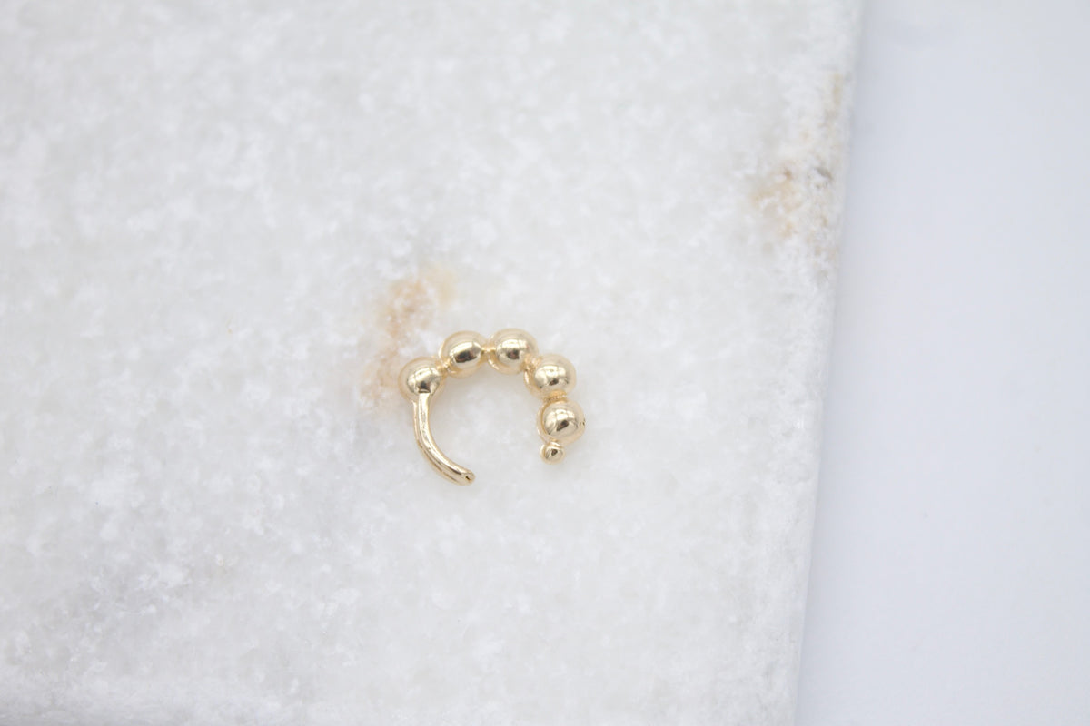 A gold beaded ear cuff rests on a white marble surface.
