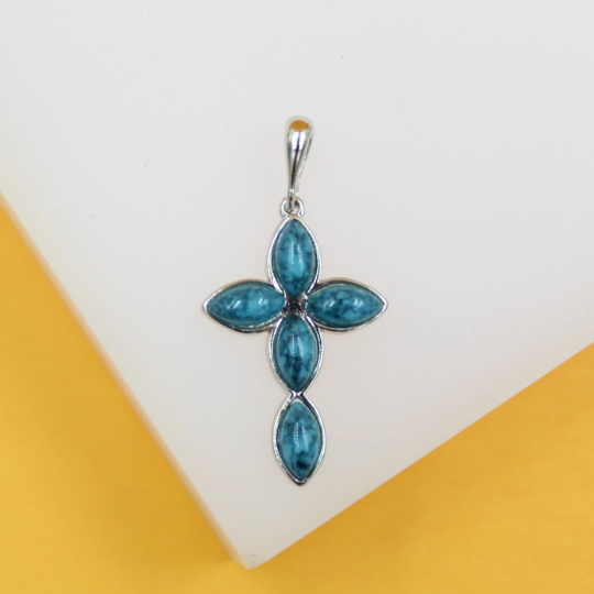 A silver cross pendant featuring marbled turquoise marquise-cut stones rests against a white display surface.
