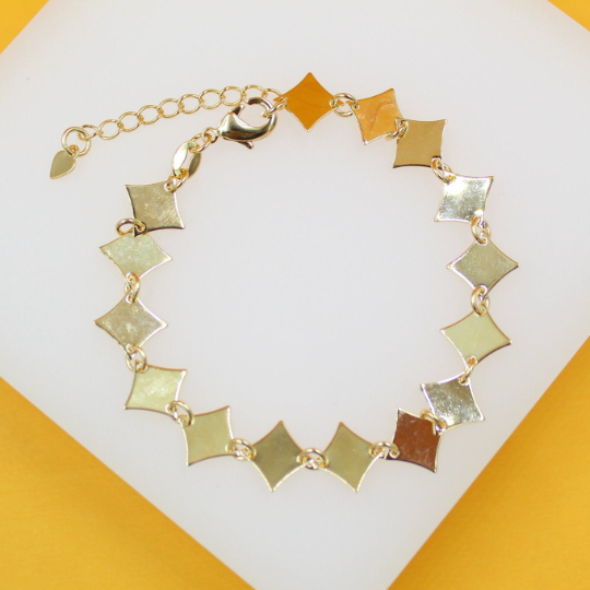 A gold link bracelet featuring geometric rhombus charms rests on a white display surface.