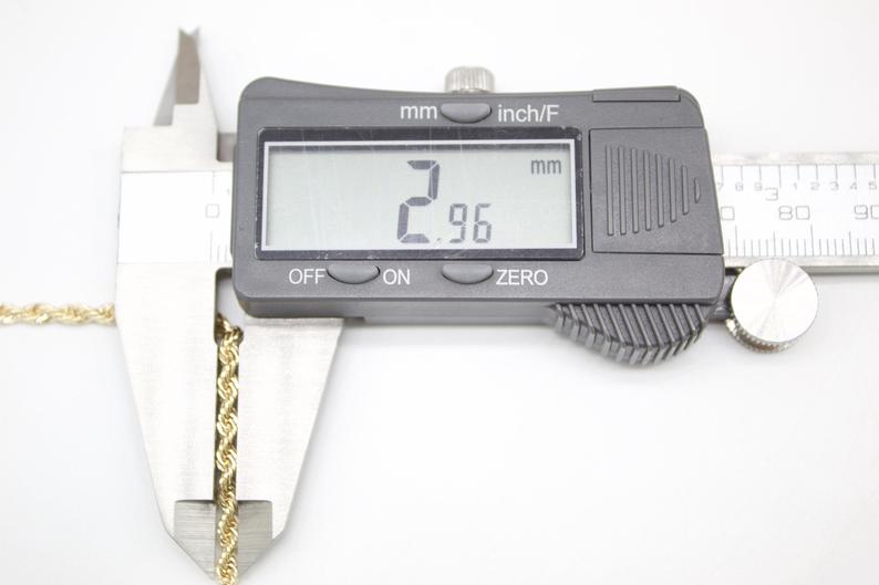 A digital caliper measures the 2.96 mm thickness of a gold rope chain necklace.