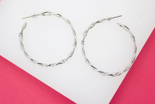 A pair of twisted silver hoop earrings rests on a white and pink surface.