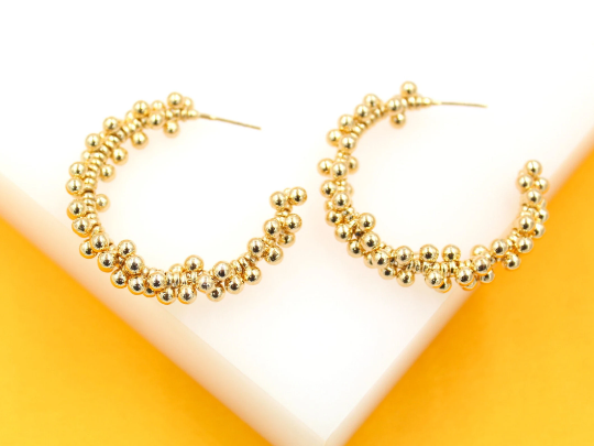 A pair of textured gold hoop earrings rests on a white display surface against a vibrant yellow background.