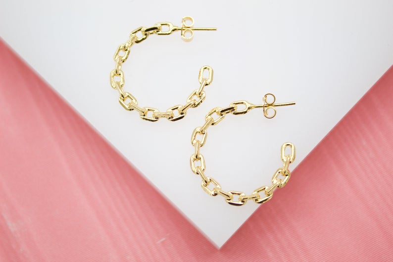 A pair of gold chain link hoop earrings rests on a white and pink display surface.