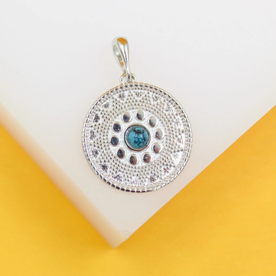 A detailed silver pendant with intricate patterns features a central turquoise gemstone.