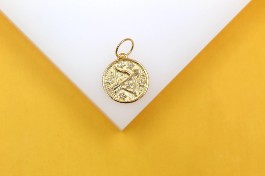 A gold Sagittarius zodiac charm with sparkling crystal accents rests on a white and yellow display stand.