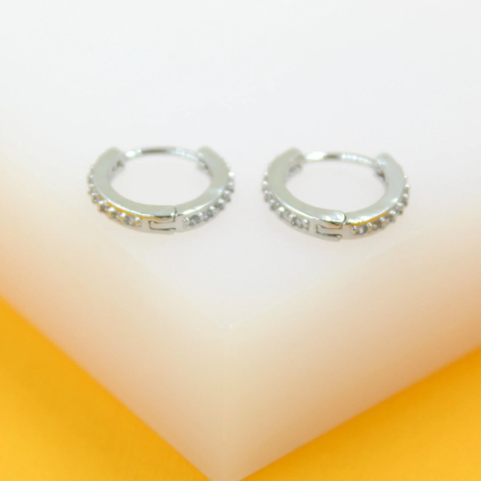 A pair of sparkling silver huggie hoop earrings with embedded crystals rests on a display stand.