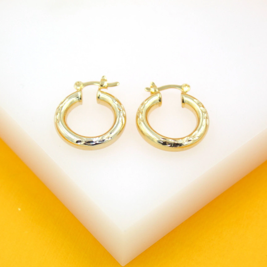 A pair of small gold hoop earrings with textured diamond-cut details rest on a white display surface.