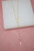 A delicate gold rosary necklace featuring white pearl beads and a hanging cross pendant rests on a white display block.
