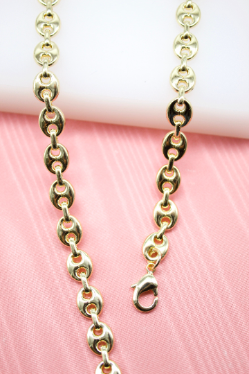 A close-up shot showcases a polished gold-plated mariner link chain necklace lying against a soft pink backdrop.