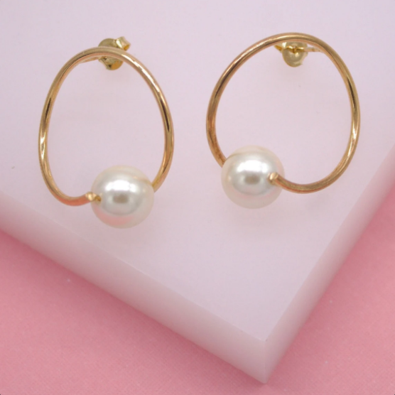 A pair of elegant gold hoop earrings featuring delicate dangling pearls rests on a soft pink surface.