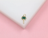 A small gold palm tree pendant featuring green enamel leaves rests on a white and pink surface.