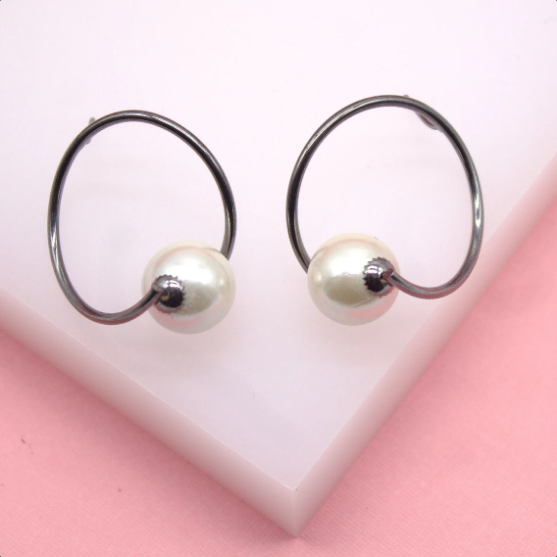 A pair of modern silver hoop earrings featuring dangling white pearls rests on a pink and white display block.