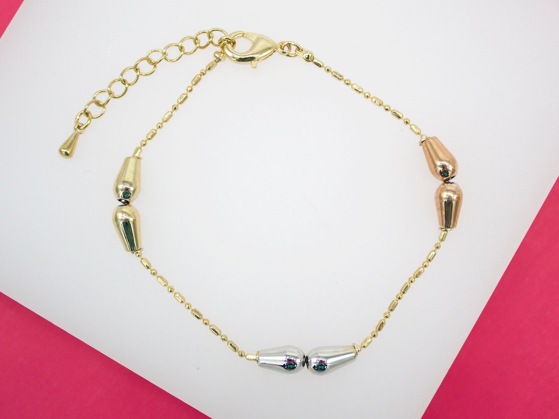 A delicate gold chain bracelet features multi-toned teardrop charms in gold, rose gold, and silver.