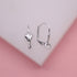 Two silver leverback earring findings with decorative fan-shaped fronts rest on a white display block against a pink background.