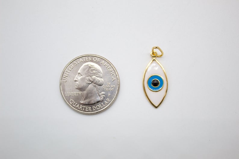 A white enamel evil eye charm rests beside a US quarter coin to show its compact size.