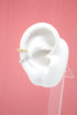 A white mannequin ear displays a textured gold and a textured silver helix ear cuff against a plain pink background.