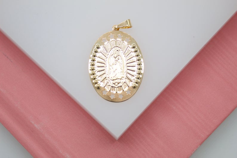 A gold Our Lady of Guadalupe pendant rests centrally on a white and pink display surface.