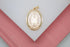 A gold Our Lady of Guadalupe pendant rests centrally on a white and pink display surface.