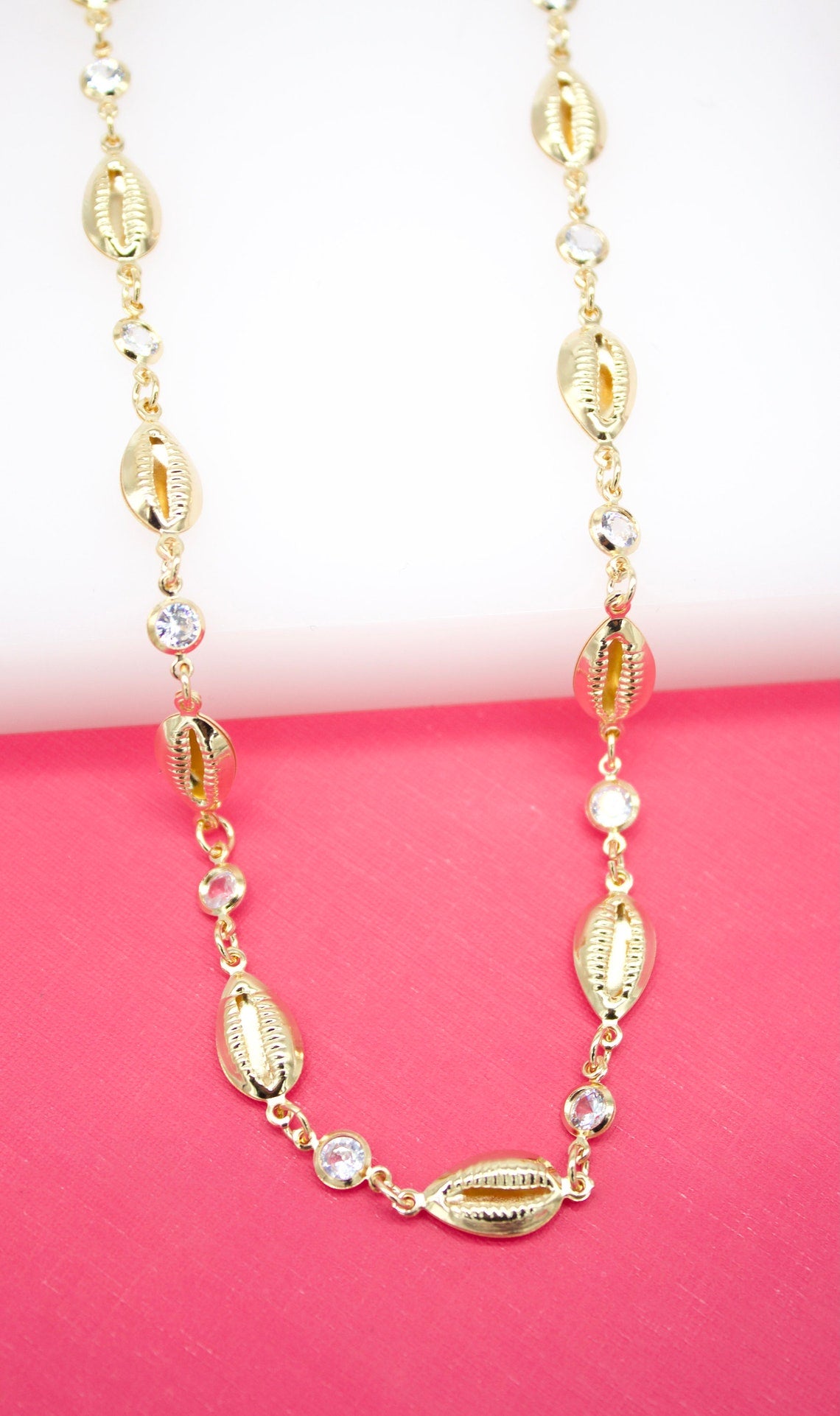A gold necklace features alternating cowrie shells and sparkling cubic zirconia stones.