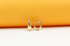 A pair of sleek gold huggie earrings rests against a vibrant orange and white background.