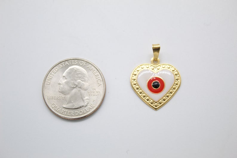 A gold heart-shaped evil eye pendant rests next to a US quarter coin for scale.