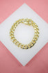 A thick gold cuban link bracelet rests on a white display block against a pink background.